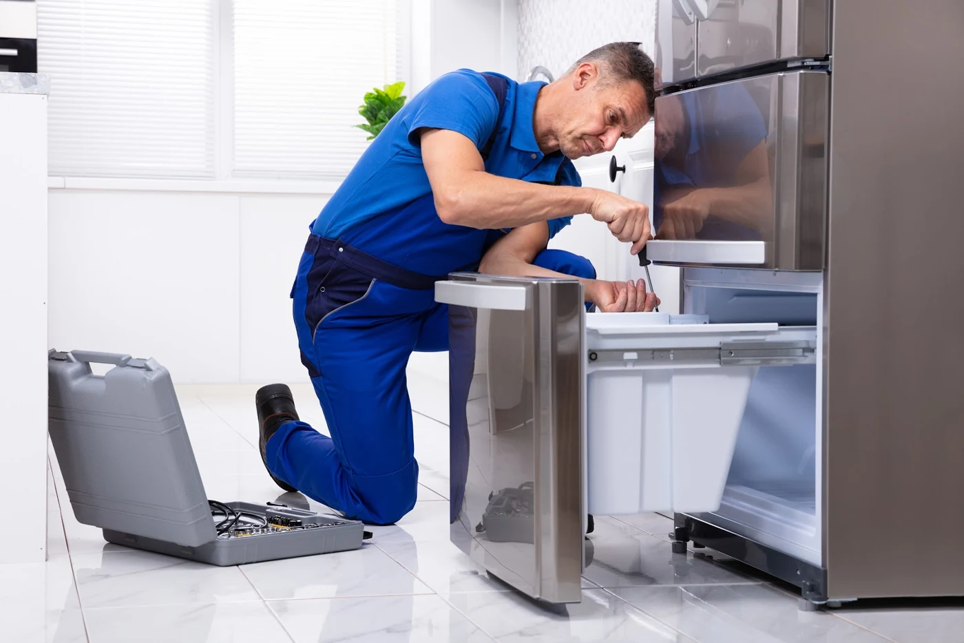 Appliance technician repairing the lower compartment of a stainless steel refrigerator