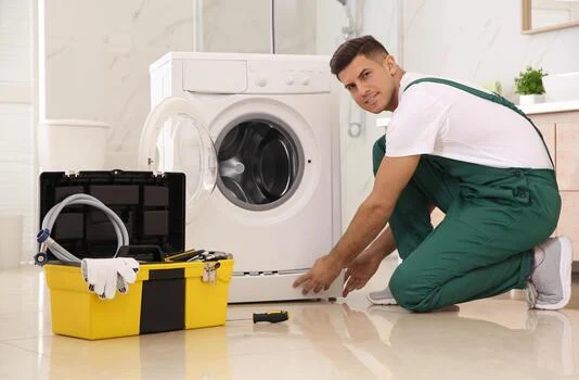 Technician working beside a front-loading washing machine with a toolbox